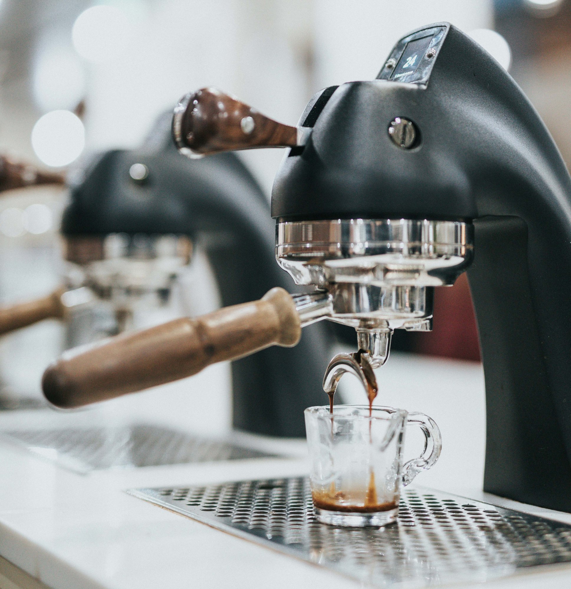 Shot of espresso being pulled from black machine with wood handles